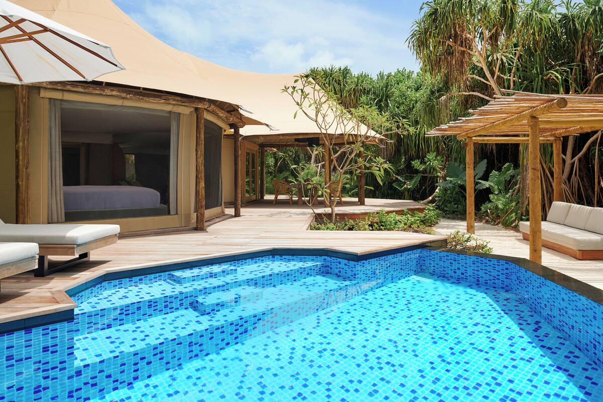 Ein Poolbereich mit blau gefliestem Pool, Holzdeck und Sitzgelegenheiten im Freien.