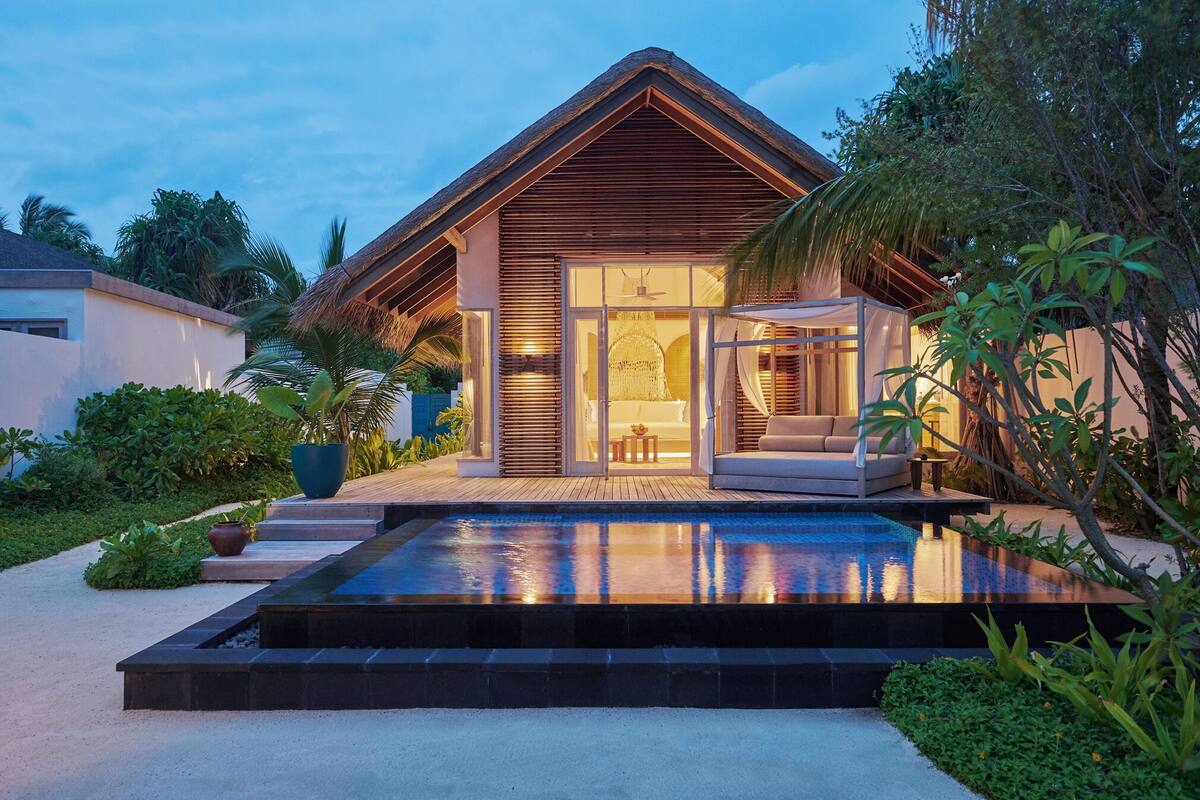 Eine moderne Villa mit Swimmingpool, überdachter Sitzgruppe und üppiger tropischer Bepflanzung.