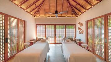 Traditional-style room with two beds, ceiling fan, and large window with a wooden lattice design.