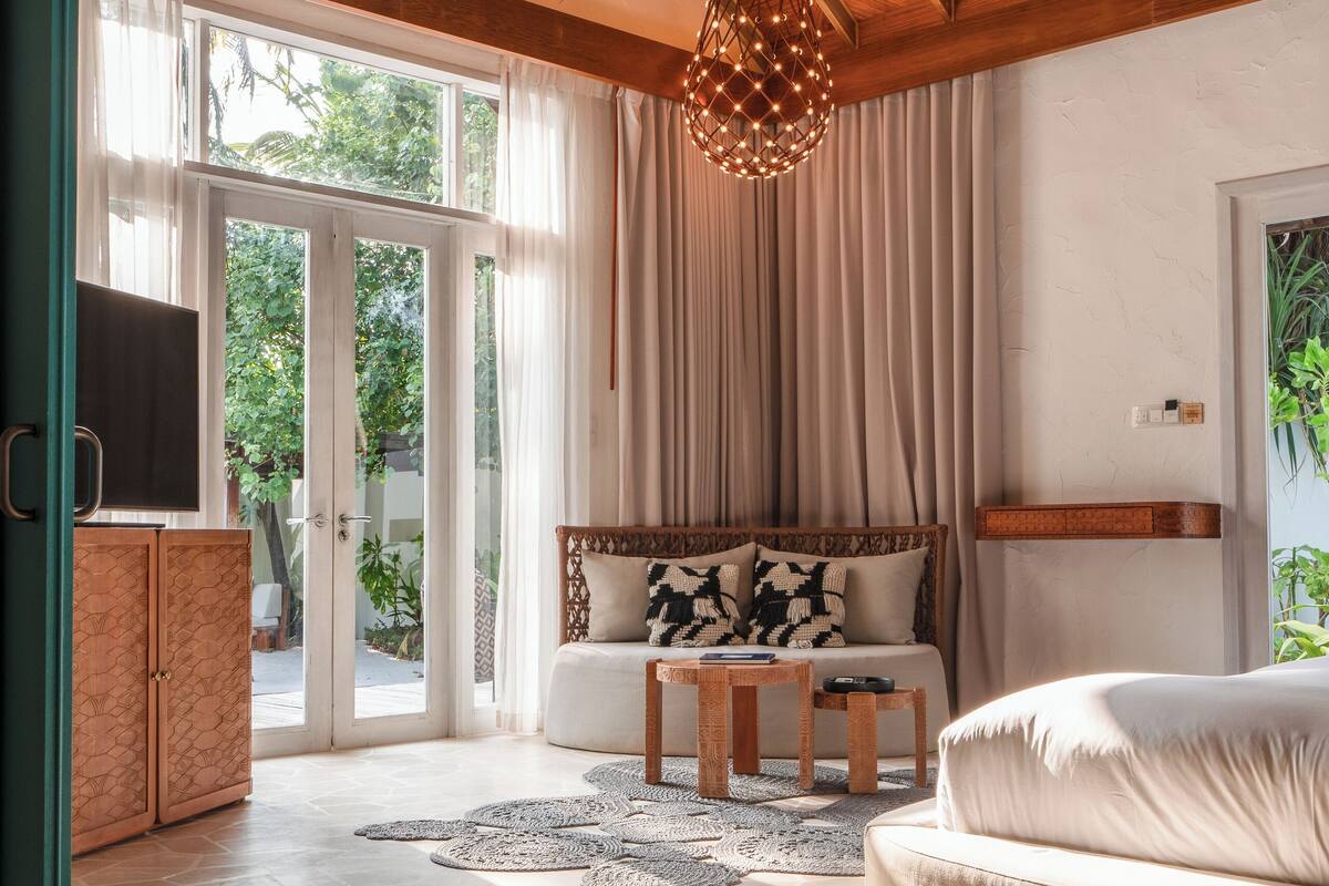 Ein geräumiges Wohnzimmer mit Holzboden, einem großen Fenster, einem Sofa, einem Couchtisch und einem Fernseher.