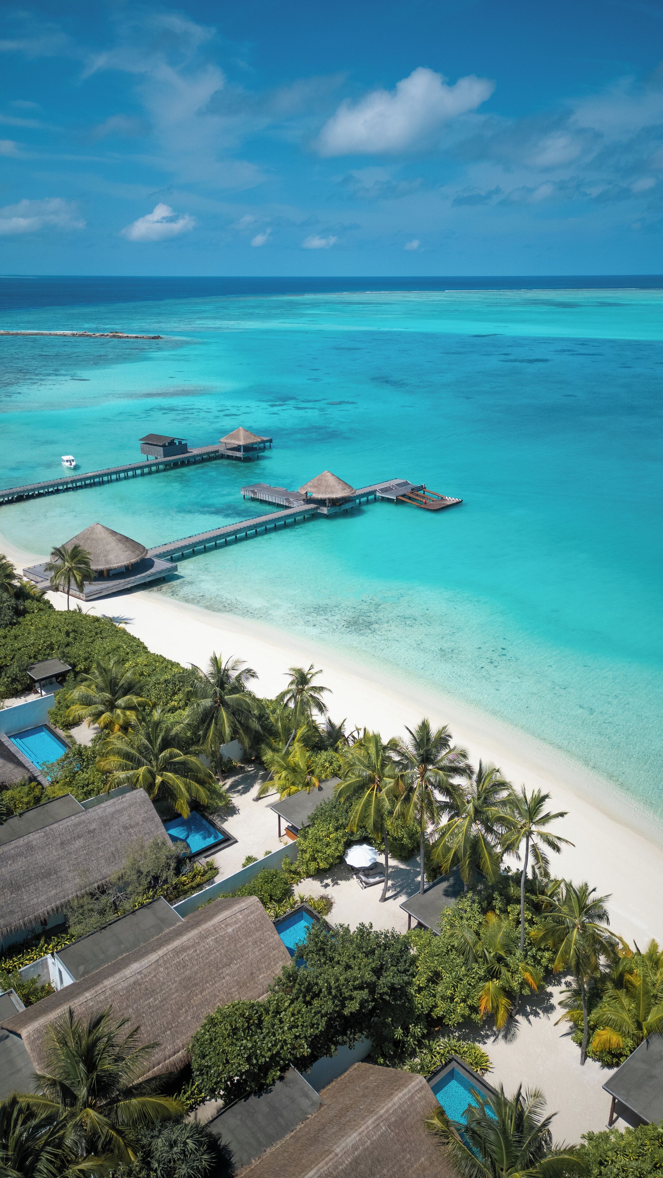 An aerial view of a tropical resort with overwater bungalows, a beach, and clear turquoise waters.