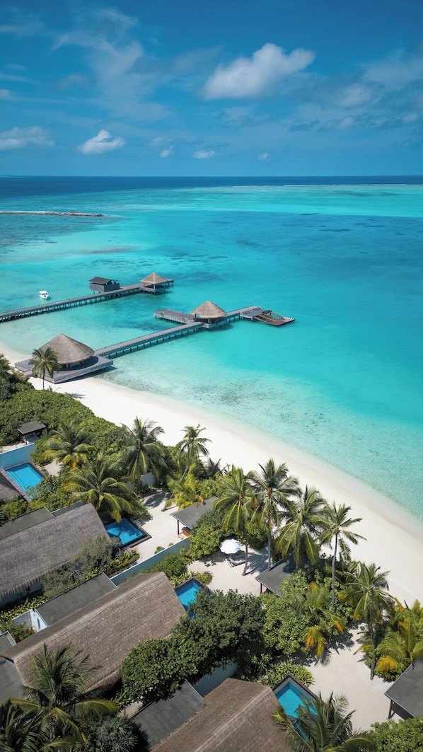 An aerial view of a tropical resort with overwater bungalows, a beach, and clear turquoise waters.