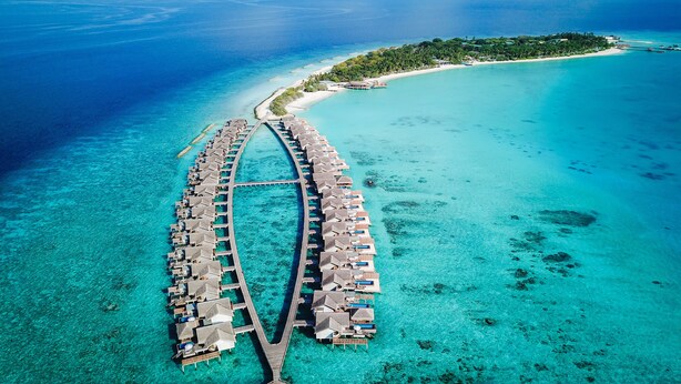 Luftaufnahme eines Resorts mit überwasser Bungalows, die über einen zentralen Steg verbunden sind.