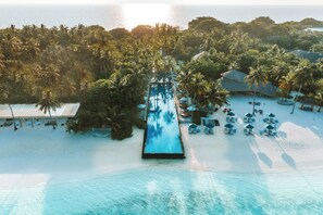 Vue aérienne d’un complexe hôtelier avec une longue piscine, des palmiers et des chaises de plage.