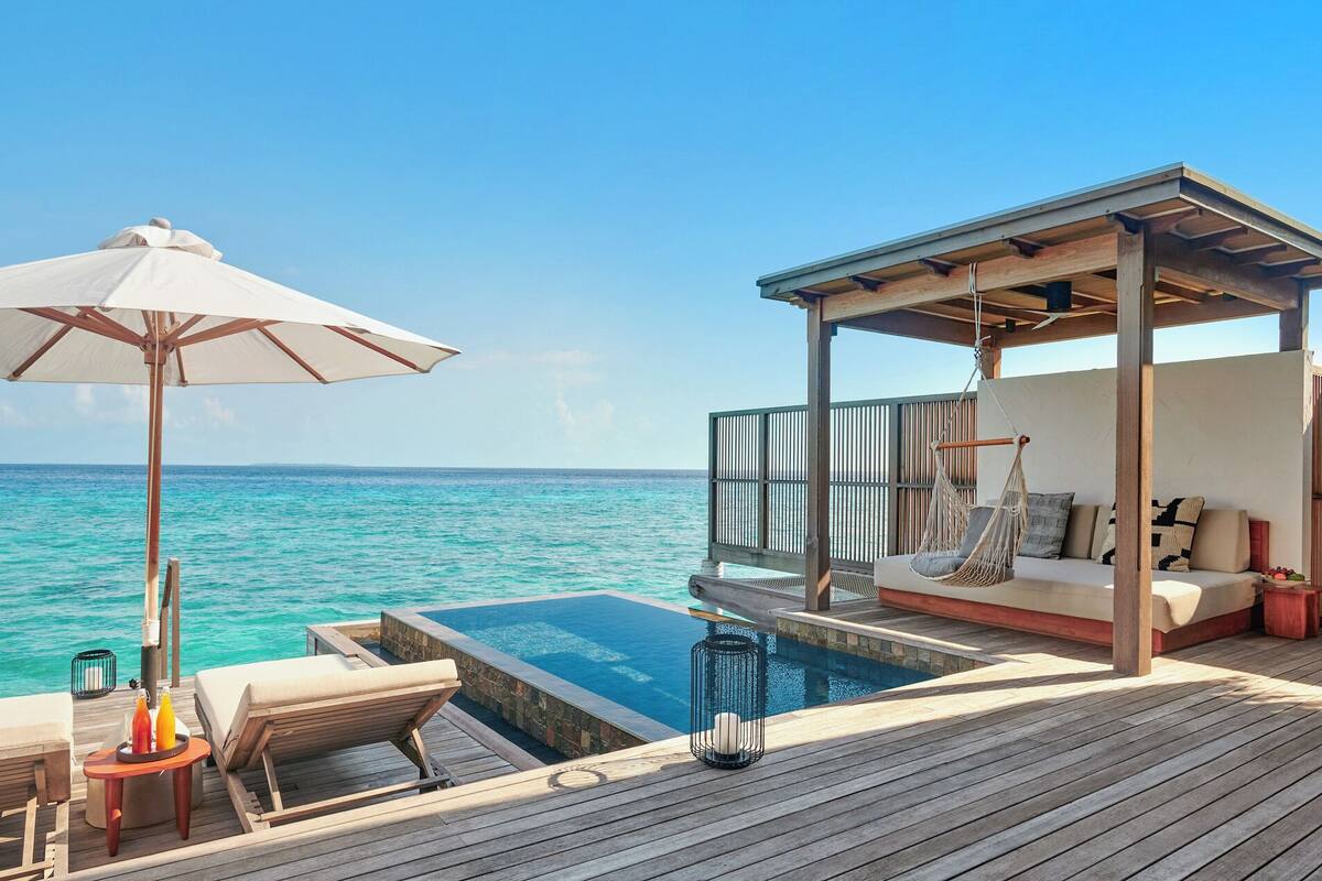 Ein Infinity-Pool mit Holzterrasse, einer Hängematte und einer überdachten Sitzgruppe mit Kissen.