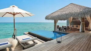 Ein Pool ohne Rand mit Holzterrasse, einer Struktur mit Reetdach und Blick auf den Ozean.