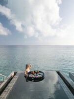 Mulher relaxando perto de uma mesa à beira da piscina, com uma refeição preparada, com vista para o oceano.