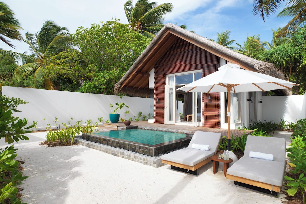 Eine moderne Villa mit Pool, Liegestühlen und einem Reetdach.