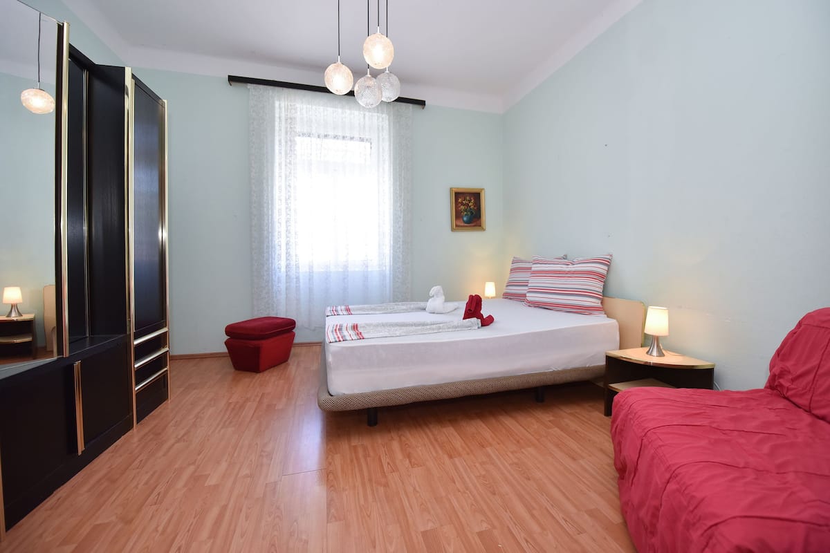 Ein Hotelzimmer mit einem Bett, einem roten Hocker, einem Nachttisch mit Lampe und einem Kleiderschrank.