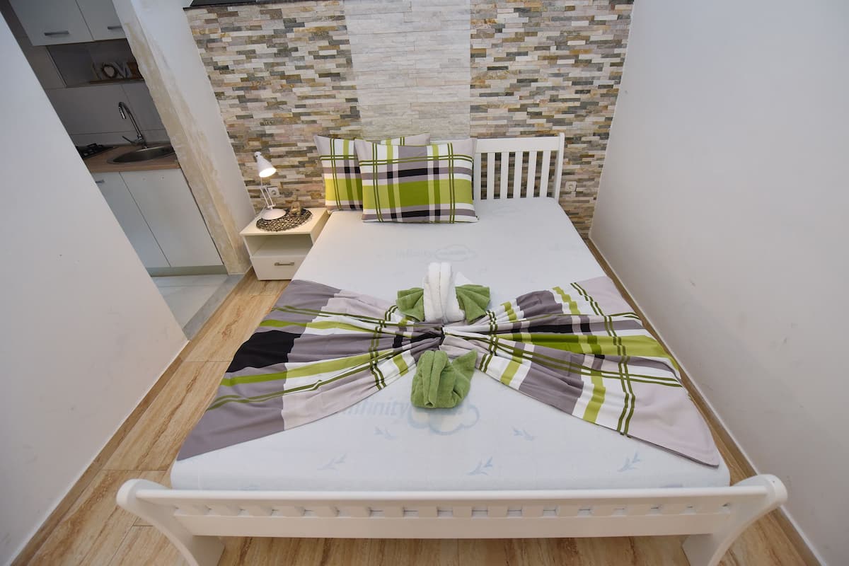 Ein ordentlich bezogenes Bett mit gestreifter Decke und Kissen, eine Nachttischlampe und eine Wand mit Mosaikmuster.