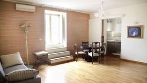 A spacious living area with a wooden floor, a sofa, a dining table with chairs, a staircase, and a kitchen visible through an open door. - Gramsci Apartments (Naples)