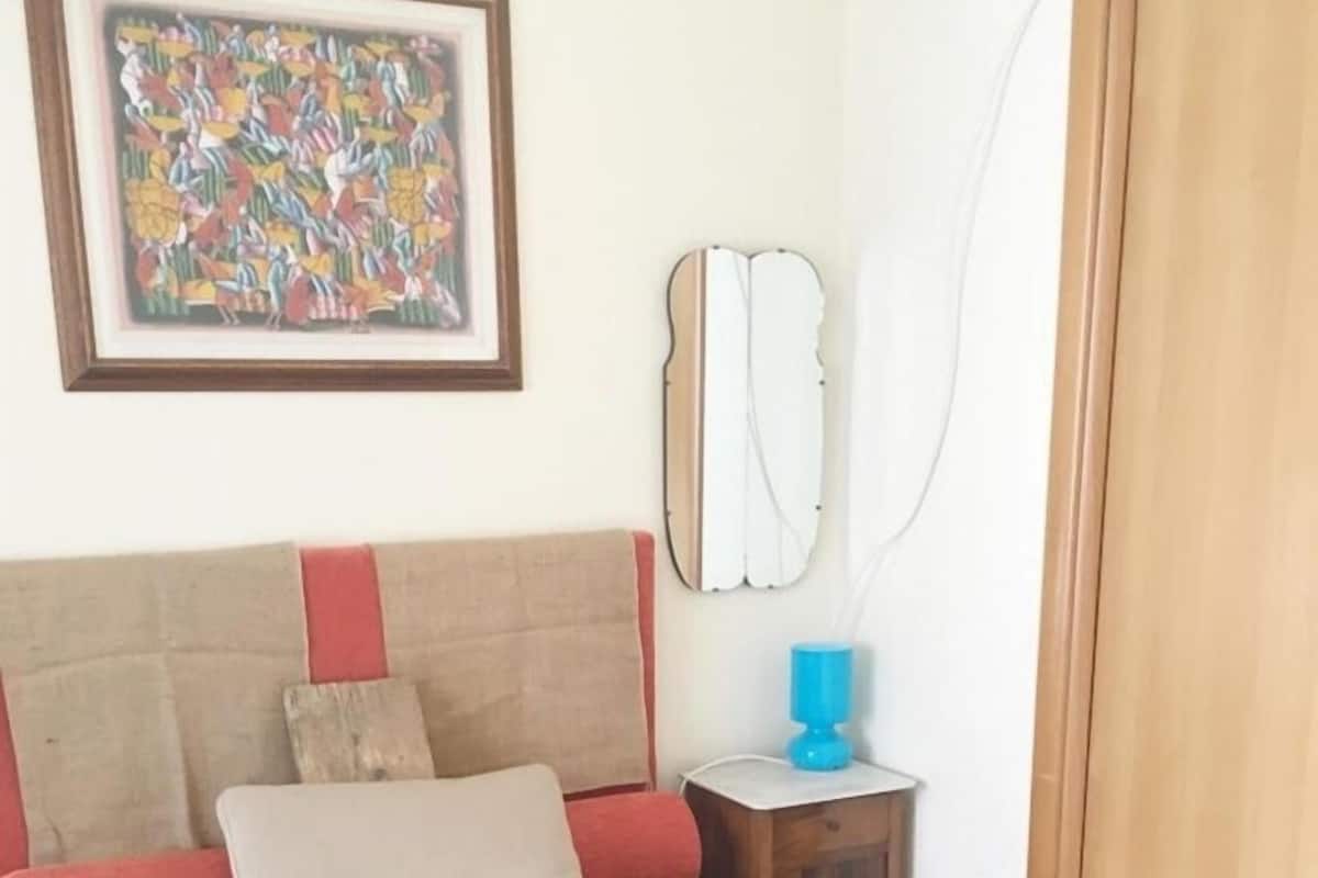 Un dormitorio con cama, almohadas, mesita de noche, espejo y un cuadro en la pared.
