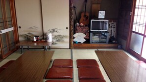 Una habitación con esteras de tatami, mesas y bancos de madera, una guitarra y decoración tradicional japonesa.