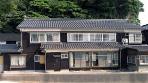 Un edificio tradicional japonés de dos plantas con tejado de tejas, ventanas grandes y puerta corredera.