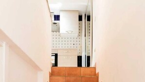 A staircase with terracotta tiles leading to a kitchen area with white cabinets and a hanging pot rack. - Luxury House (Naples)