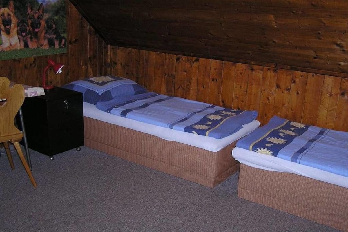 Quarto com duas camas de solteiro, uma escrivaninha e uma cadeira.