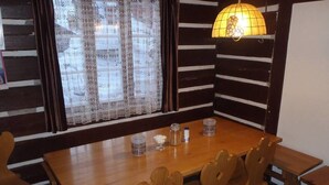 Una mesa de madera para comer con cuatro sillas, una cortina de encaje y una lámpara fijada a la pared.