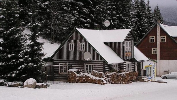 Una cabaña de madera con techo cubierto de nieve, rodeada de árboles nevados.