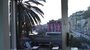 A view from a window overlooking a cityscape with buildings, palm trees, and a body of water. - Colorful Sea View Apartments (Naples)