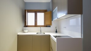 Una cocina compacta con un lavamanos integrado, una ventana sobre el lavamanos y un refrigerador.