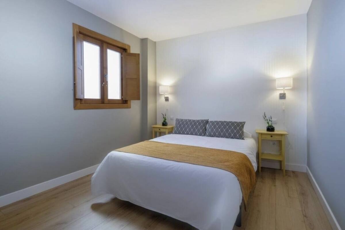 Ein Schlafzimmer mit einem Bett, zwei Nachttischen, einem Fenster und einer Wandlampe.