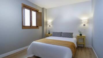 Un dormitorio con una cama, dos mesitas de noche, una ventana y una lámpara de pared.