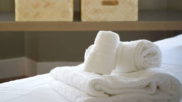 A neatly made bed with folded white towels and two storage boxes on a wooden shelf.