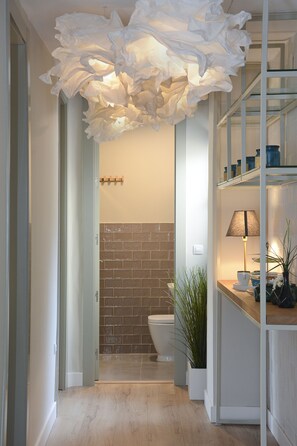 Une salle de bain moderne avec une douche, des toilettes et un lavabo. On y trouve un grand élément décoratif blanc au plafond et une étagère sur laquelle sont disposés divers objets.