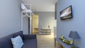 Una sala moderna con un sofá gris, un televisor montado en la pared, una lámpara y una mesita con flores.
