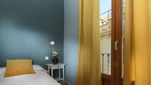 Una habitación de hotel con una cama, una mesita de noche, una lámpara y un ventanal con cortinas.