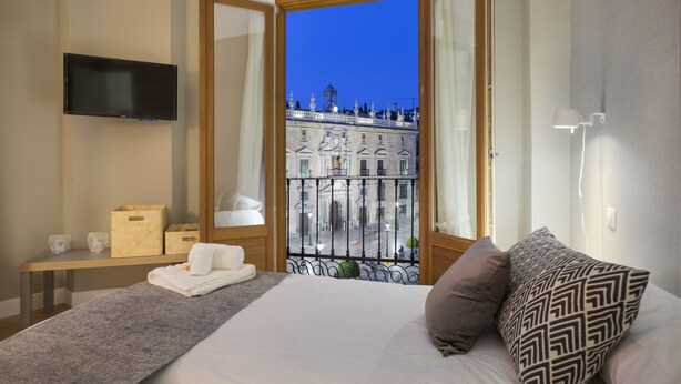 Habitación de hotel con cama, televisión y balcón con vistas a un edificio histórico.