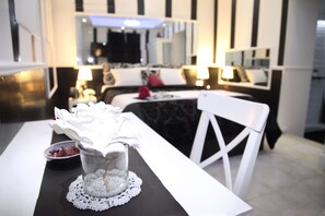 A modern hotel room with a dining area featuring a white table, a glass vase with white flowers, and a black and white striped wall. - Sermoneta Apartments (Naples)