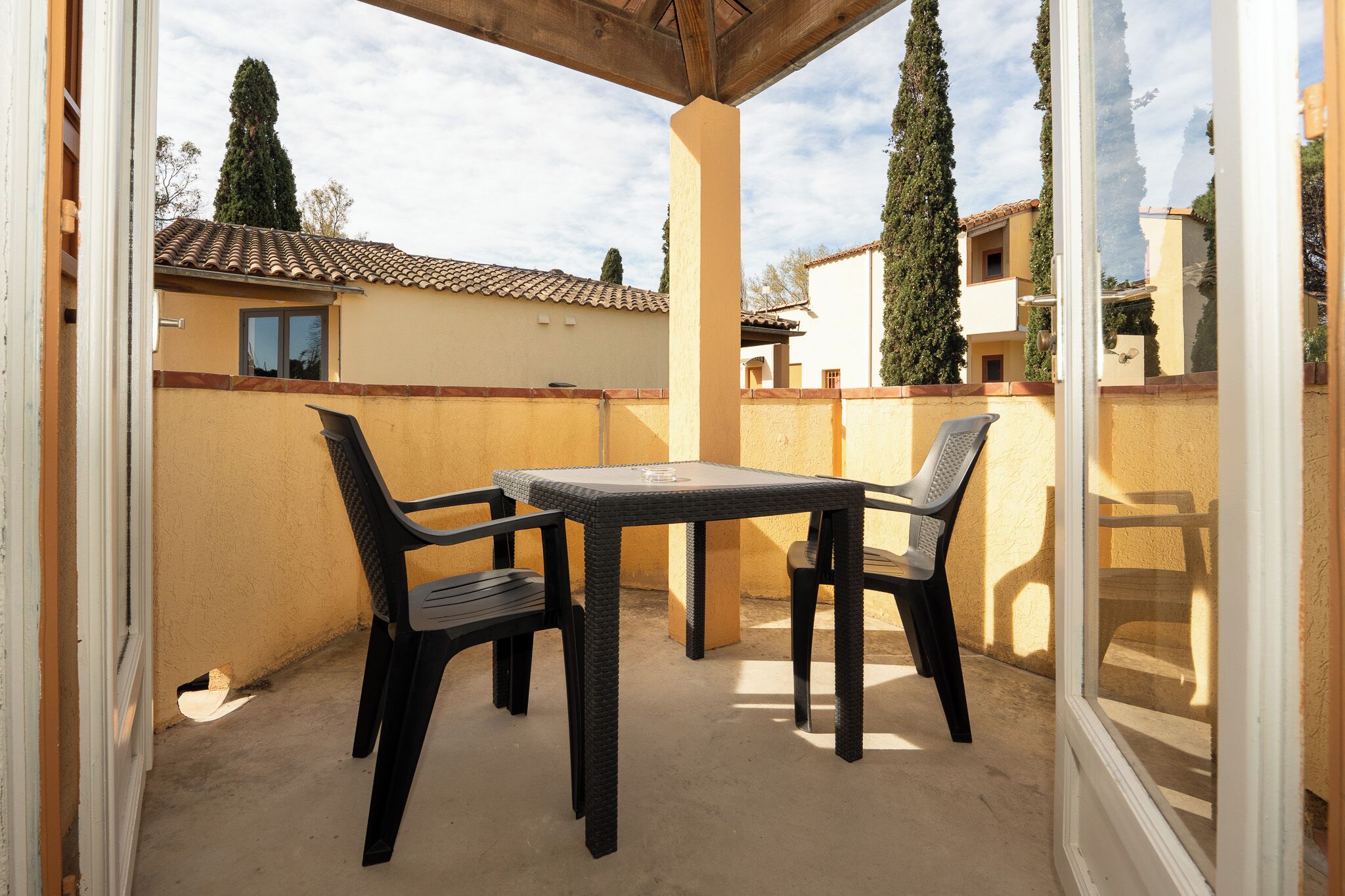 A covered patio with a table and chairs, a view of neighboring buildings, and a clear sky.