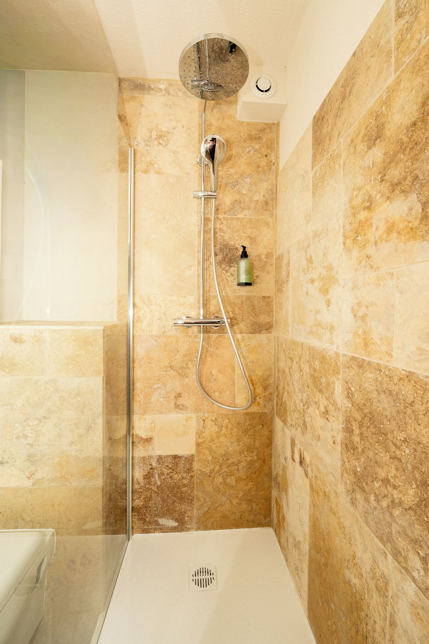 Une douche avec une porte en verre, un pommeau de douche amovible et un panneau de commande fixé au mur.