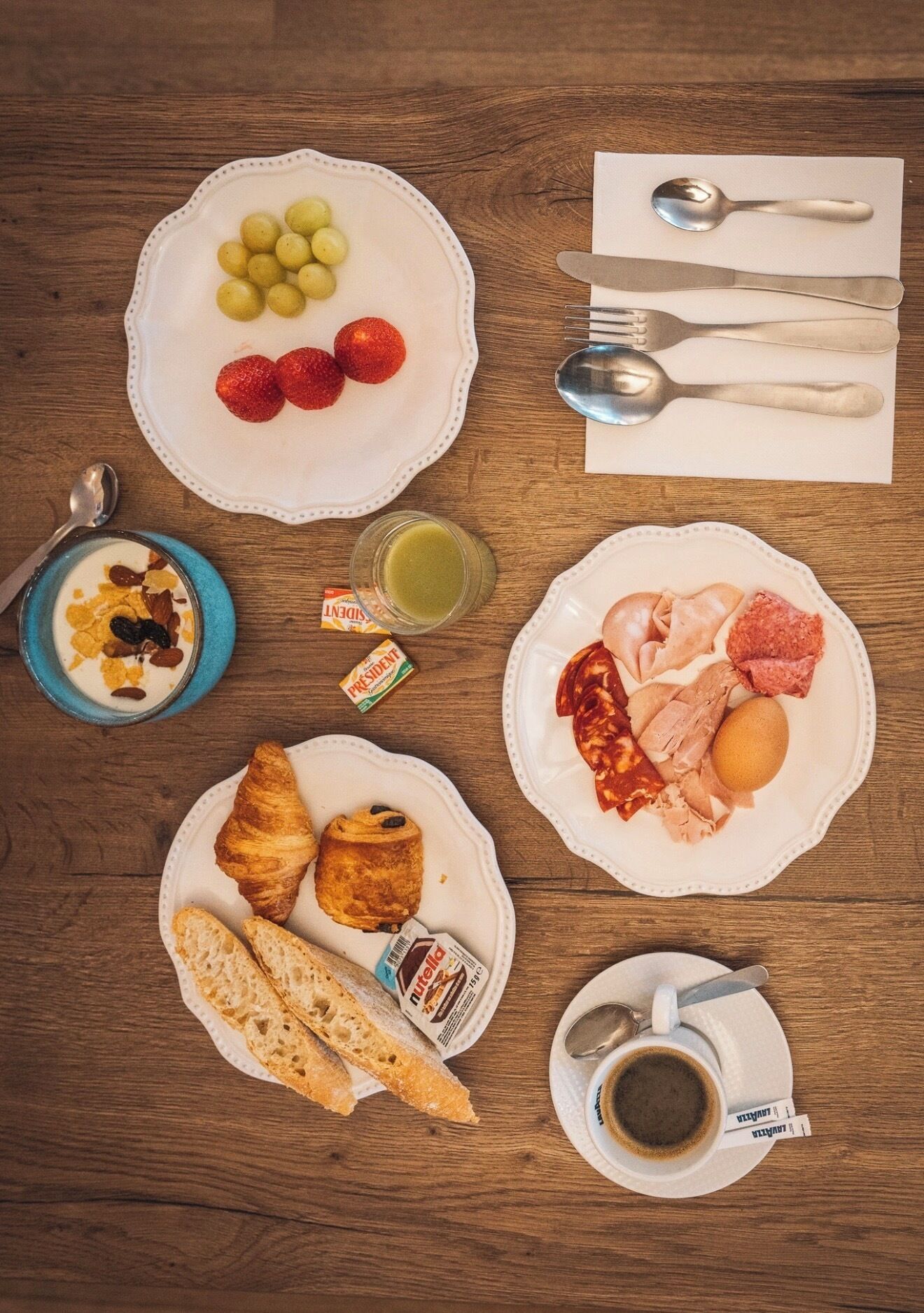 A breakfast setting with plates of food, utensils, and a cup of coffee on a wooden table.