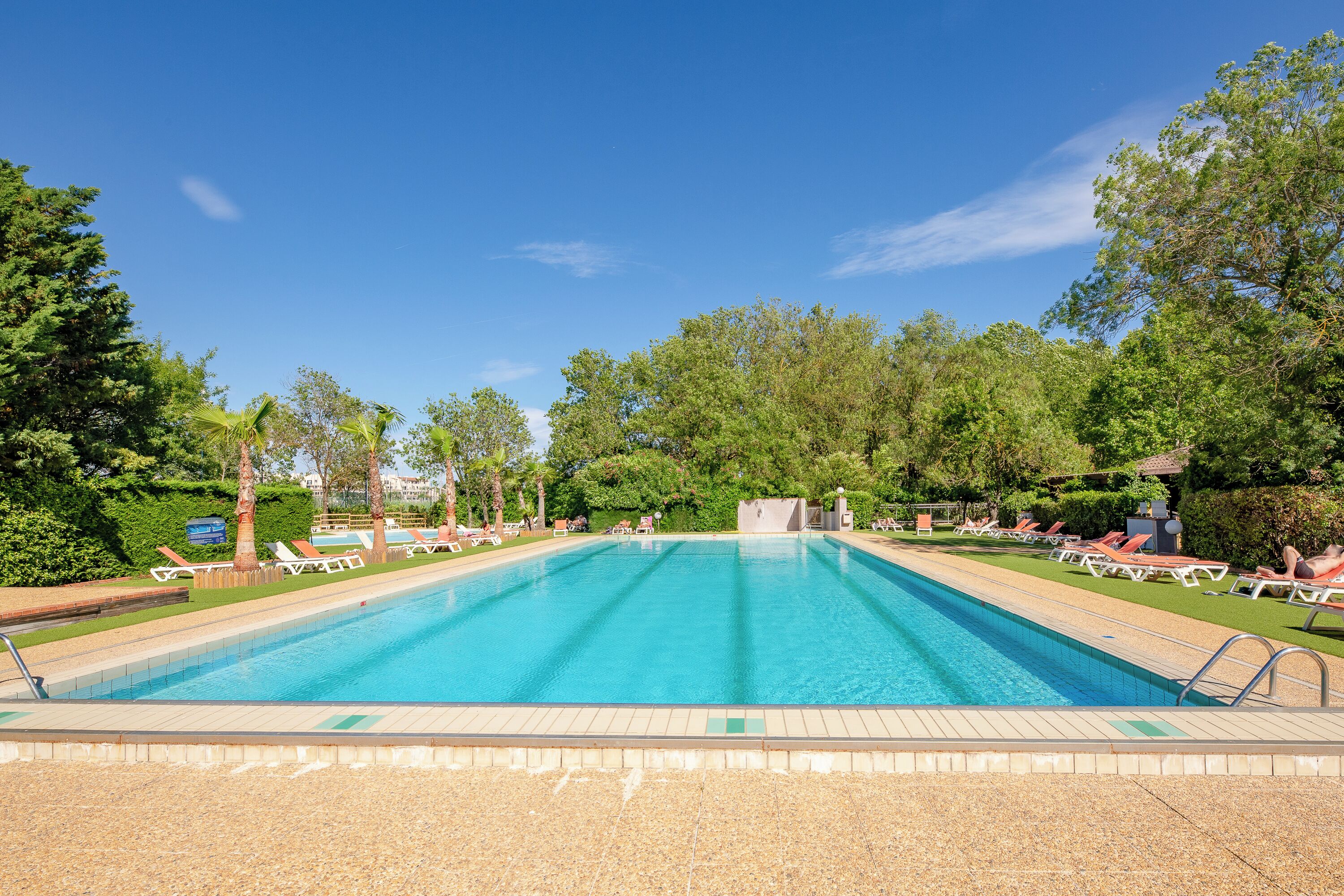 Ein rechteckiger Swimmingpool mit klarem, blauem Wasser, umgeben von einer gefliesten Liegefläche und Liegestühlen.