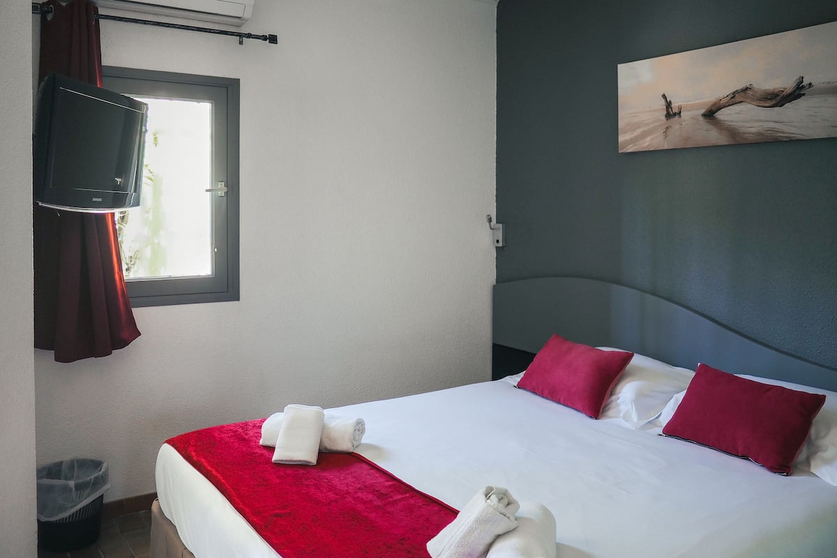 Ein Hotelzimmer mit einem Bett, roten und weißen Kissen, einer roten Tagesdecke und einem Bild an der Wand.