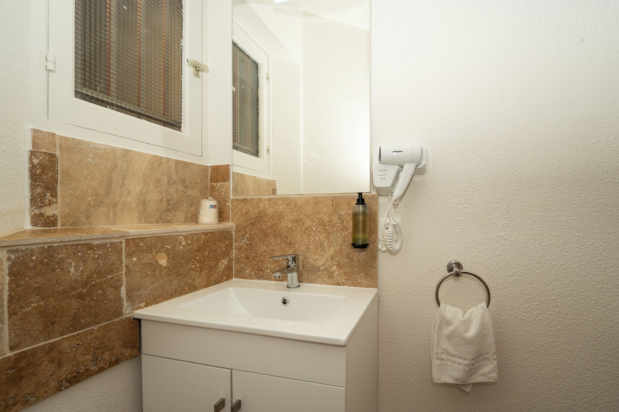Ein Badezimmer mit Waschbecken, Spiegel, Handtuchhalter und einem an der Wand montierten Föhn.