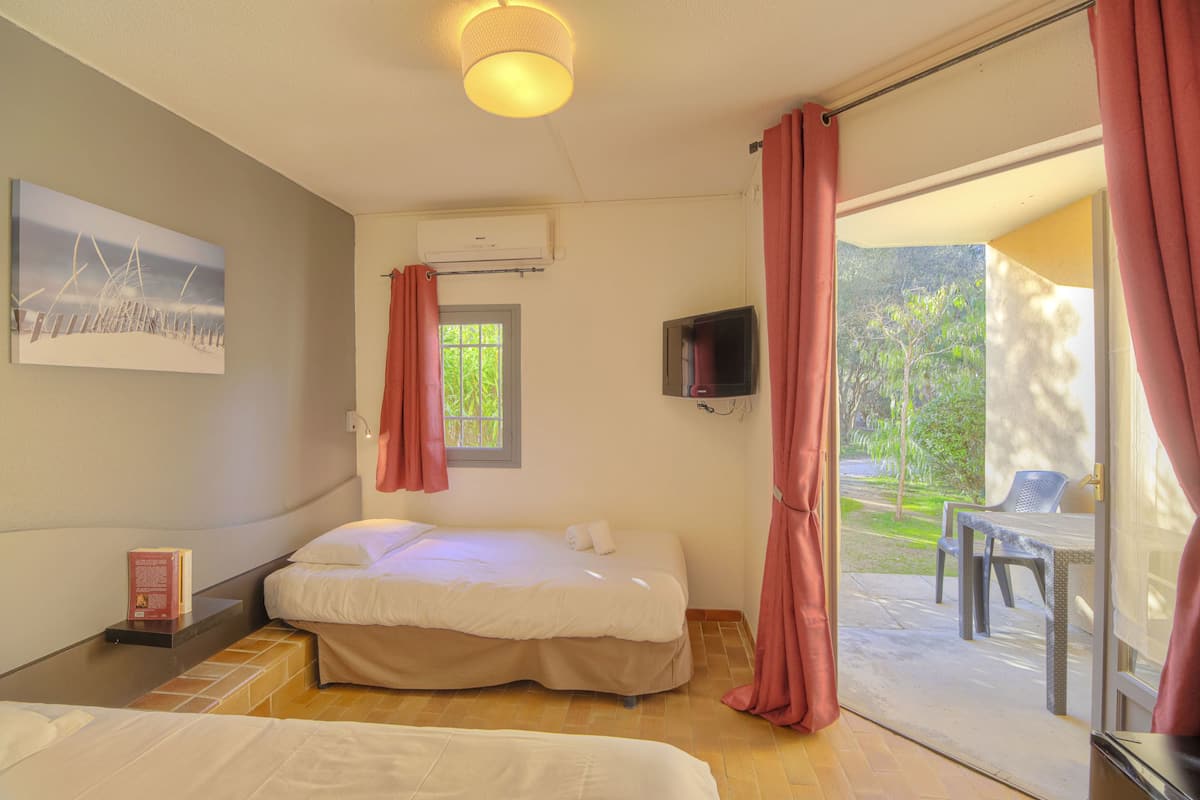 Ein Schlafzimmer mit Bett, Fernseher, Fenster und Blick ins Freie.