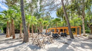 An outdoor seating area with chairs and tables, surrounded by trees and a building with a wooden structure. - Marina Hotel Club (Cogolin)