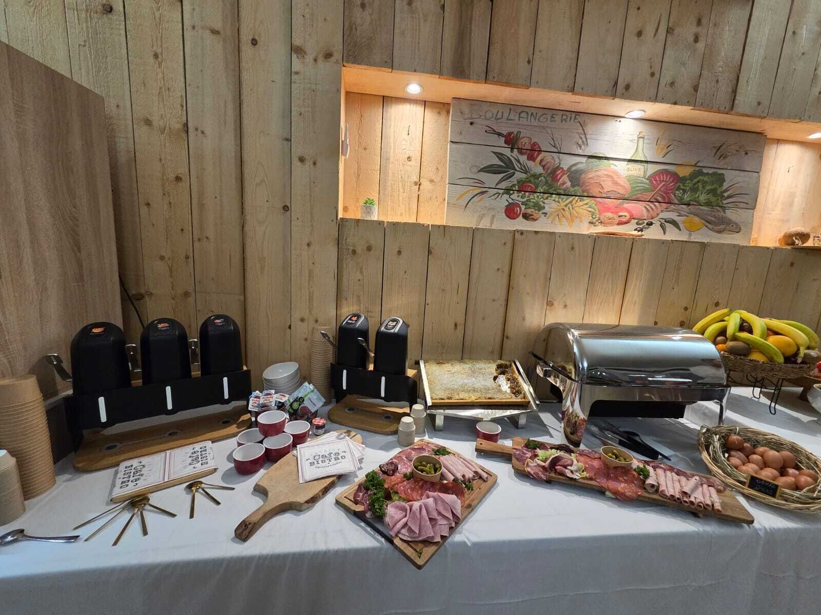 A buffet setup with various food items, including meats, cheeses, and fruits, arranged on a table with a wooden backdrop and a floral painting above.