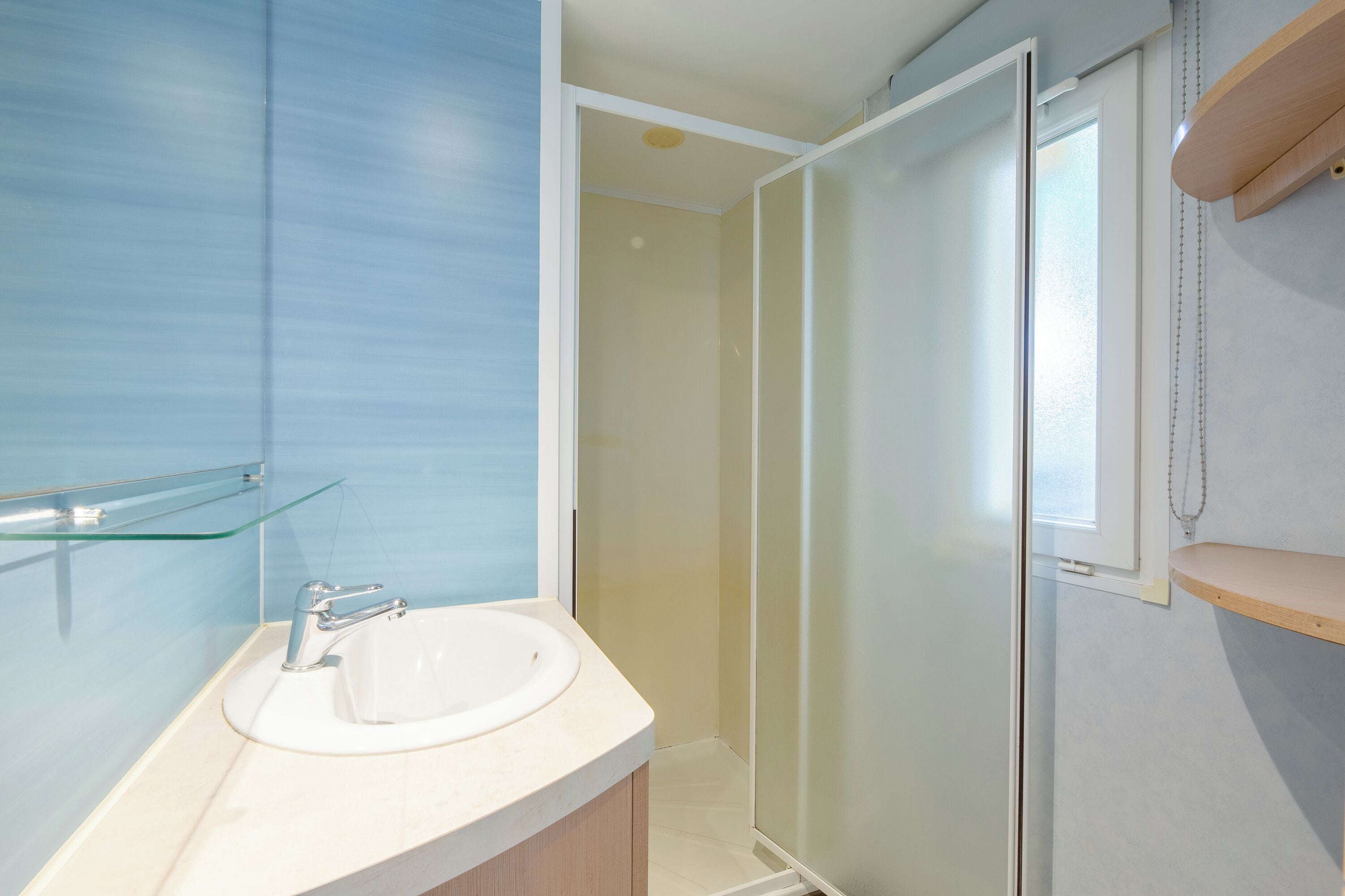 Une salle de bain avec un lavabo blanc, une étagère en verre et un espace douche.