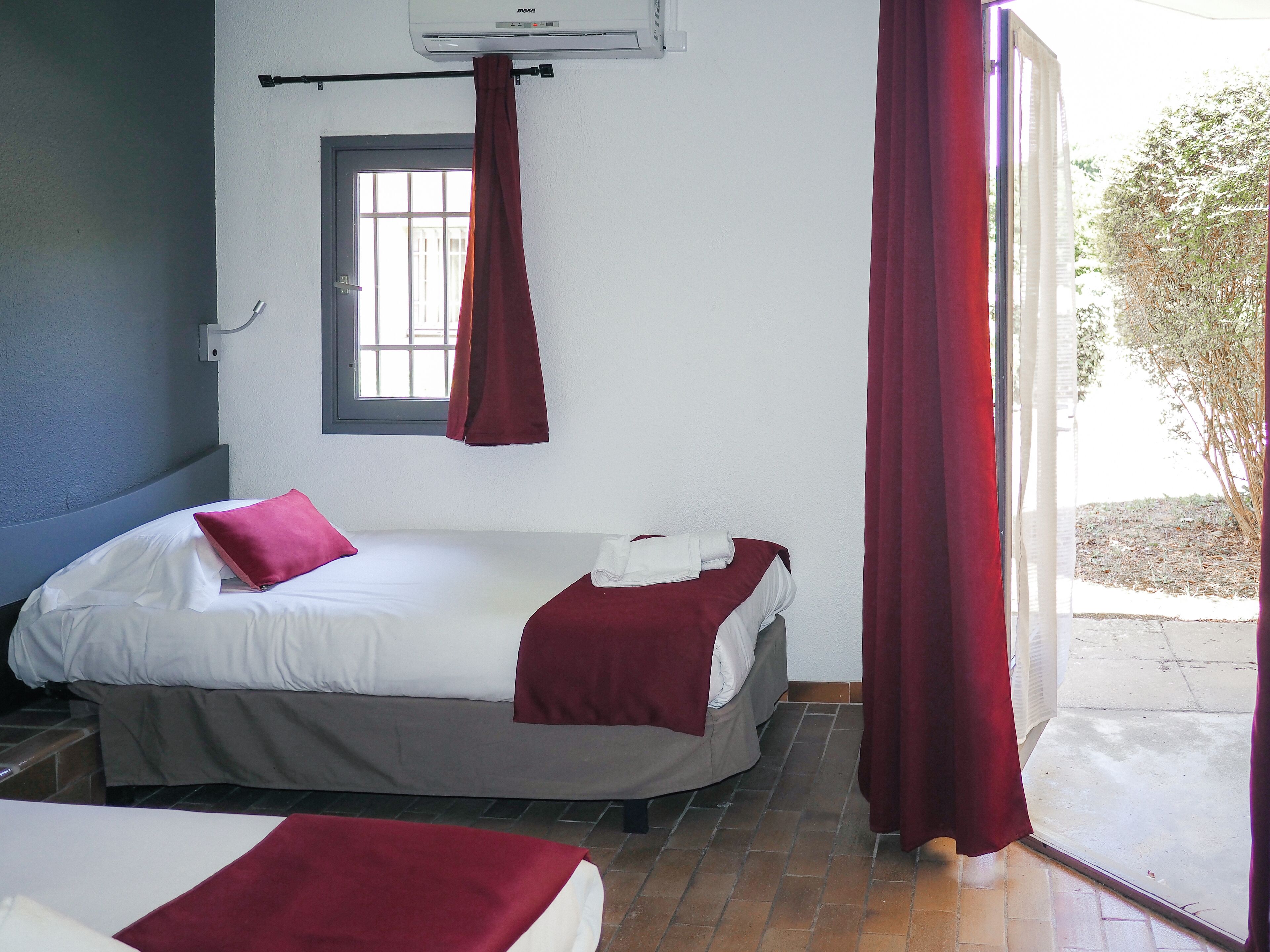 Una habitación con dos camas, una ventana con cortinas y una puerta que da al exterior.