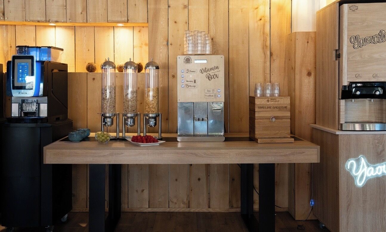 A wooden bar area with a coffee machine, a juice dispenser, and a refrigerator.