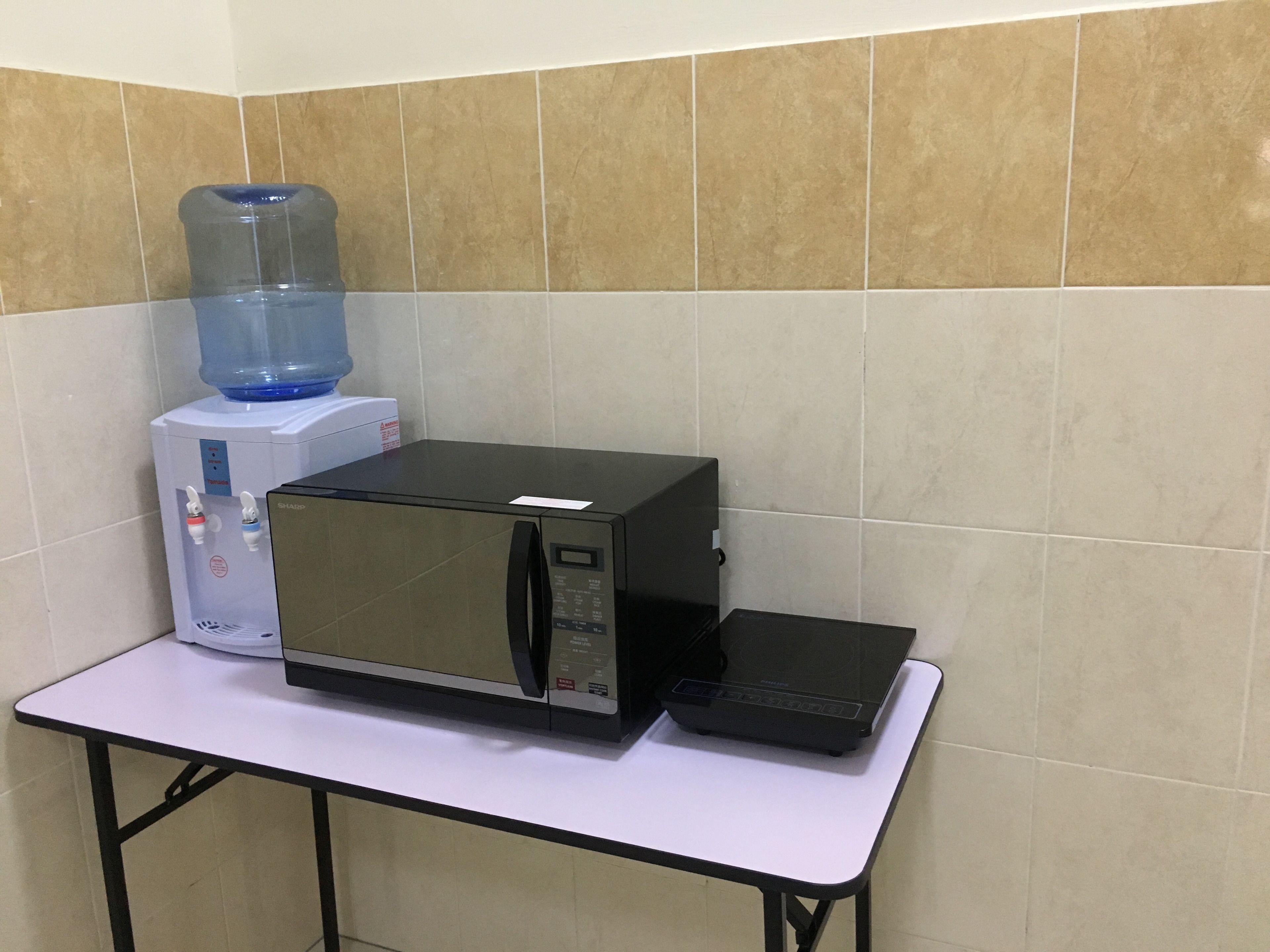A kitchenette with a microwave, toaster, and water dispenser on a white countertop.