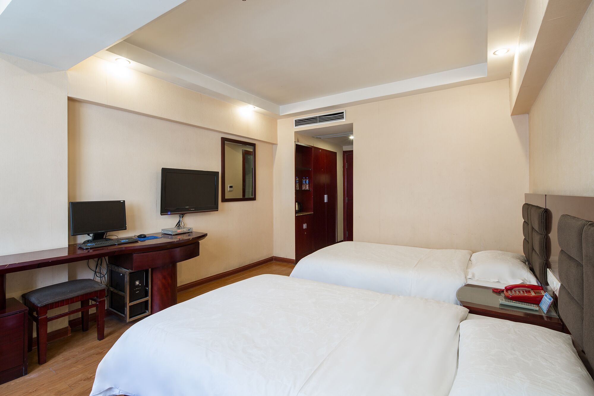 Ein Hotelzimmer mit zwei Betten, einem Schreibtisch mit Computer, einem Fernseher und einem Kleiderschrank.