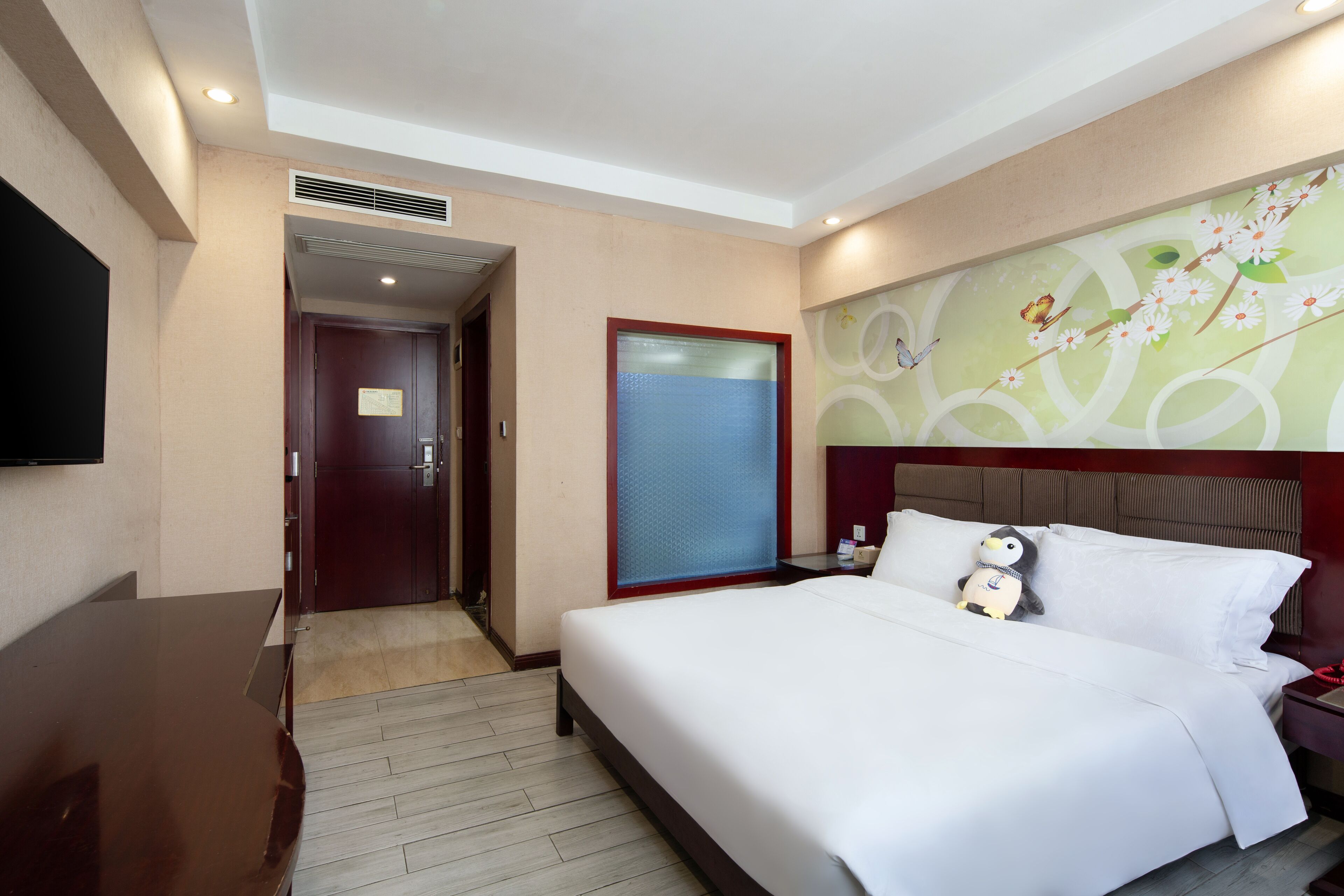 A hotel room with a large bed, a television mounted on the wall, a wooden desk, and a decorative wall mural.
