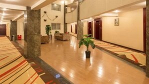 A spacious hotel lobby with a polished wooden floor, a reception desk, and a large potted plant.