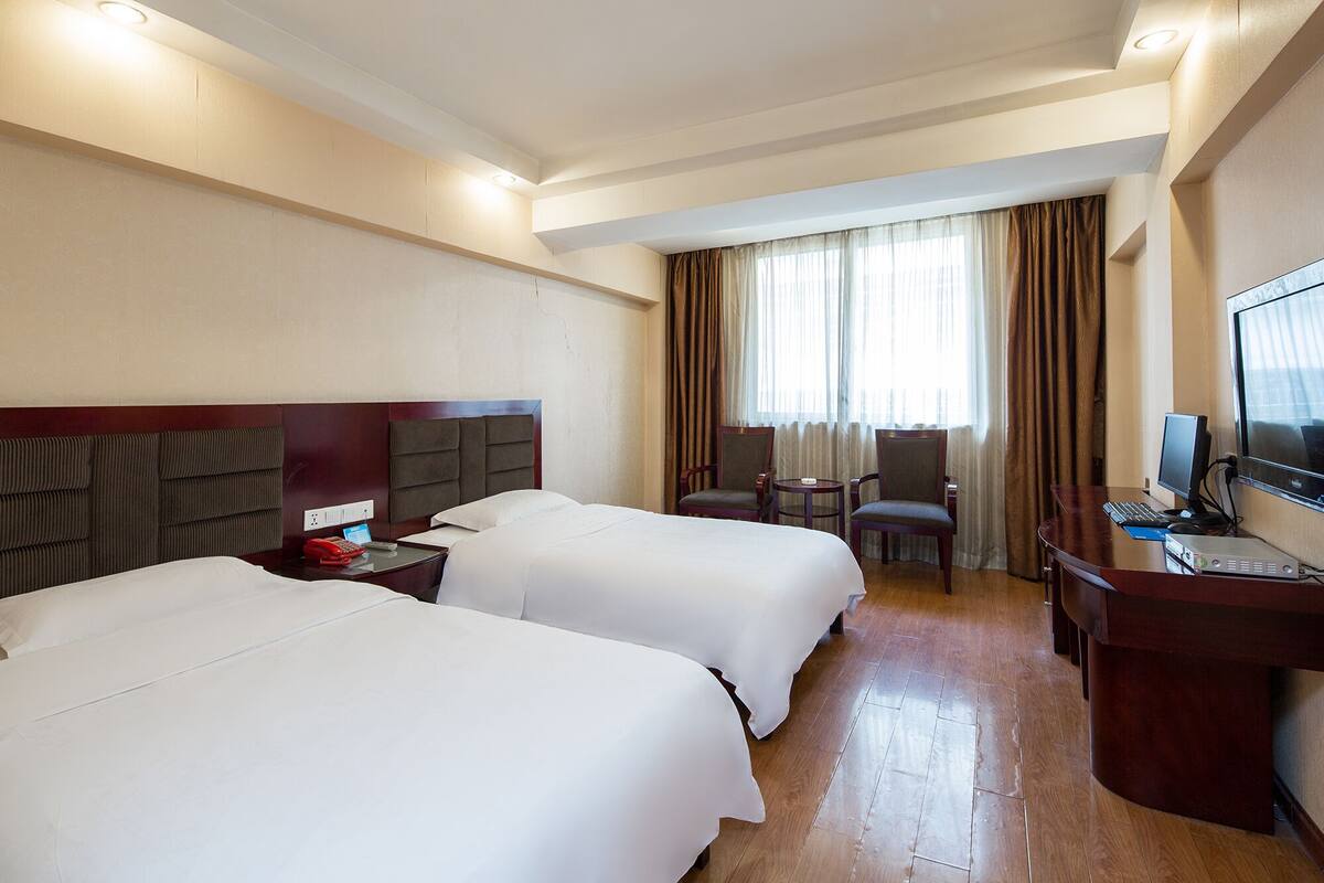 A hotel room with two beds, a desk with a computer, a chair, and a TV.