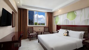 A hotel room with a large bed, two chairs, a small table, a TV, and a window with curtains.